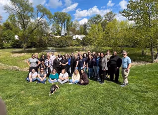 Group photo of caregivers and residents with a dog outdoors on a sunny grassy area.