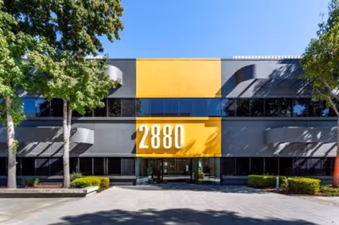 Two-story modern building with orange-yellow accents and large 2880 address plaque, trees framing entrance.