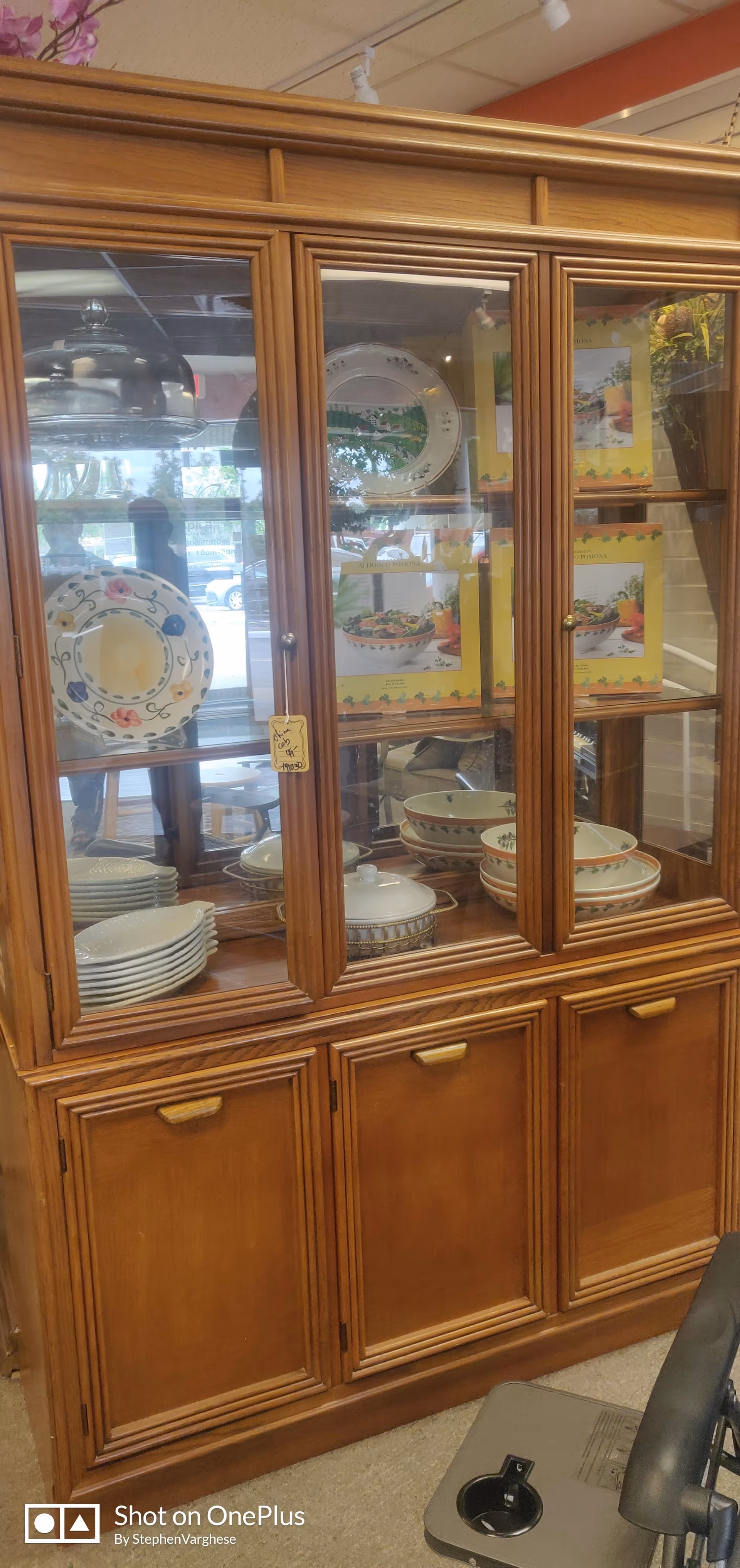 Wooden glass-front china cabinet filled with plates, bowls, and decorative dishes inside.