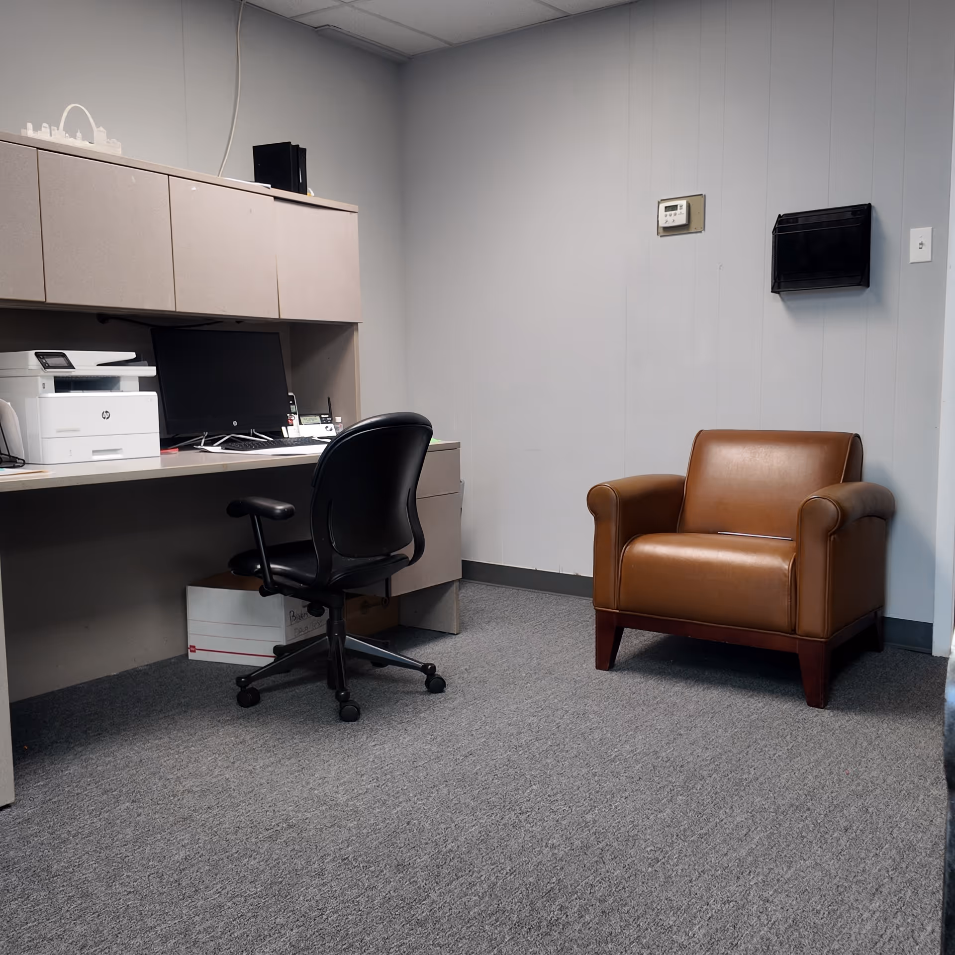 Office workspace with desk, computer, printer, and brown leather armchair.