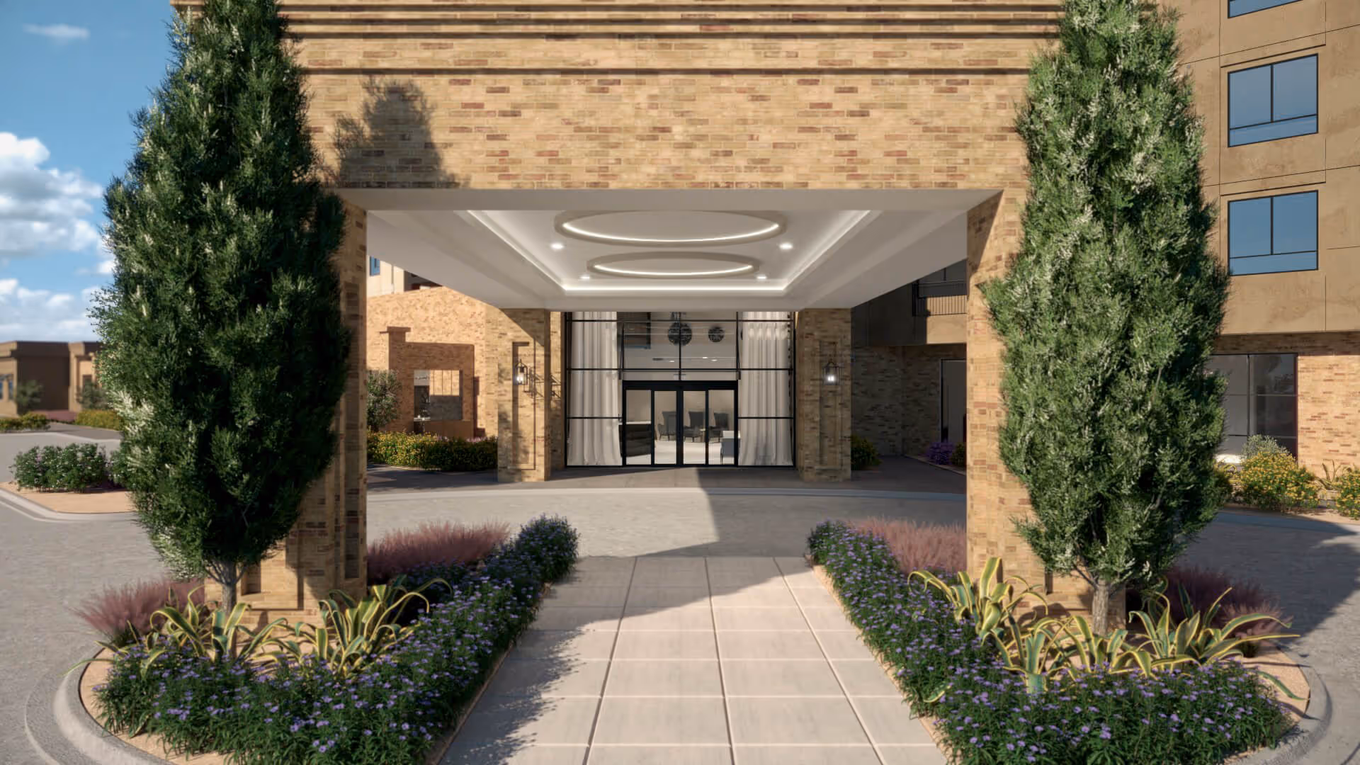 Covered porte-cochere entrance to a brick senior living building with landscaped planters and tall trees.
