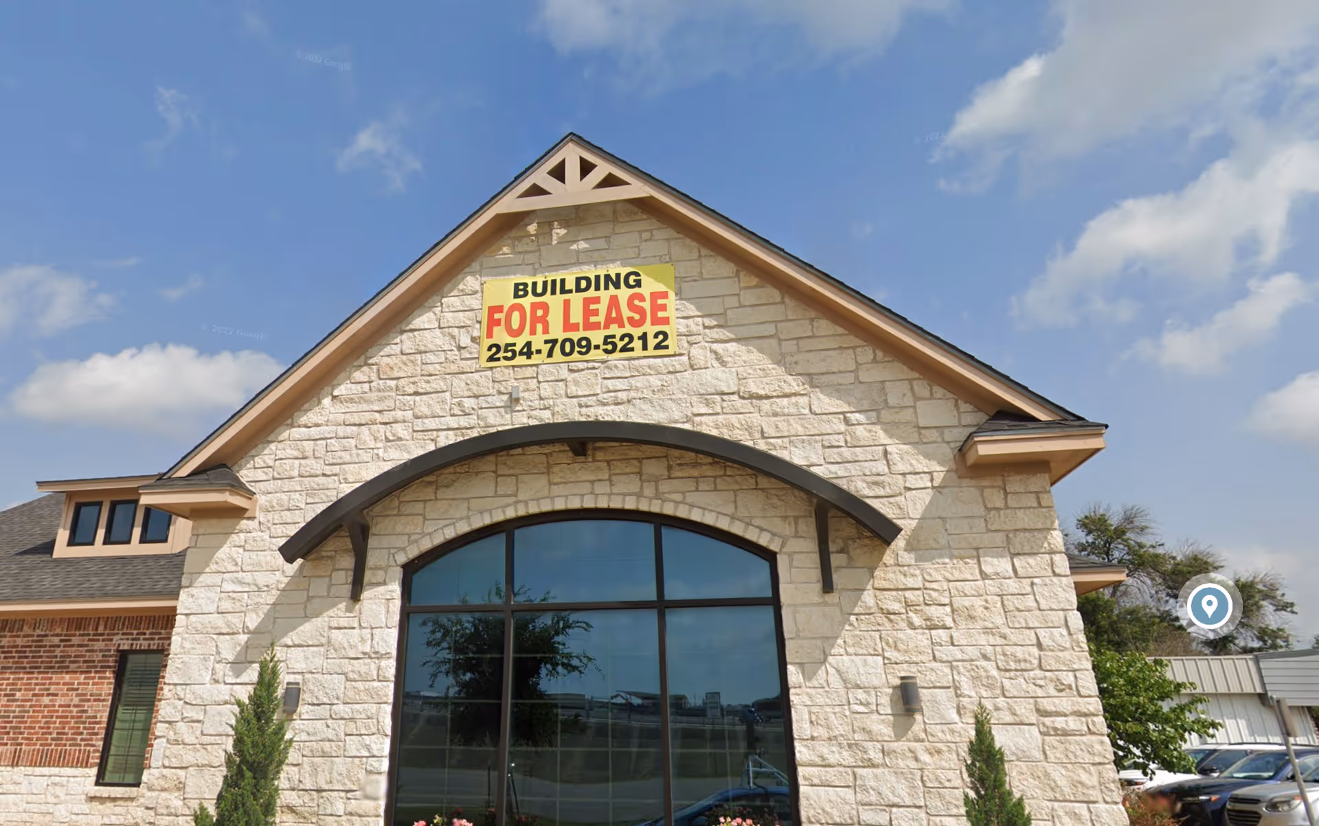 Stone-front building with a large arched window and a 'For Lease' sign.