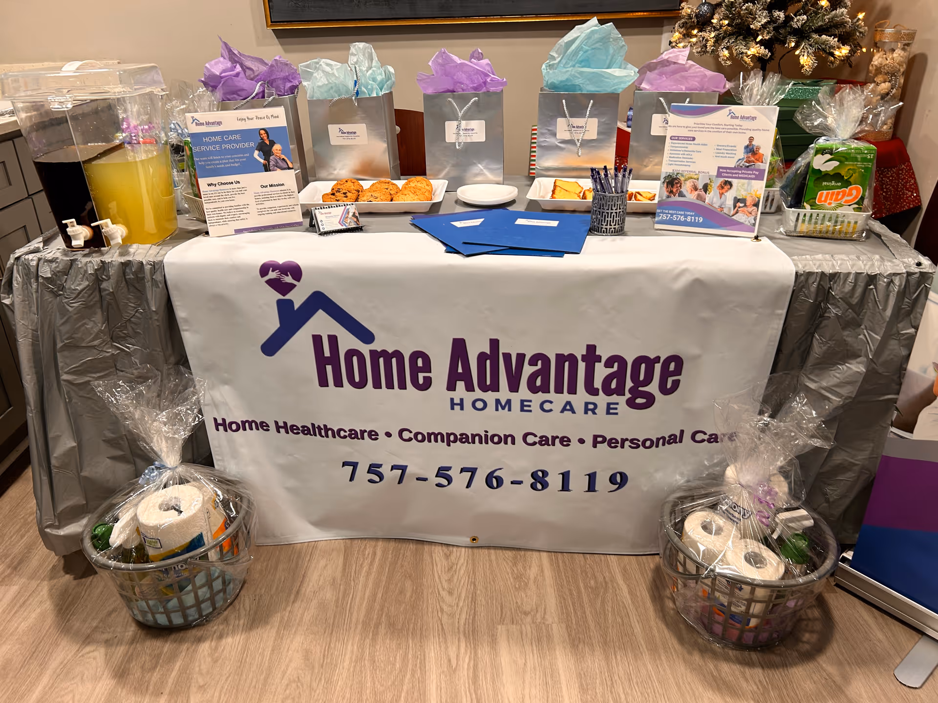 Indoor display table with Home Advantage Homecare branding, gift bags, snacks, and brochures.