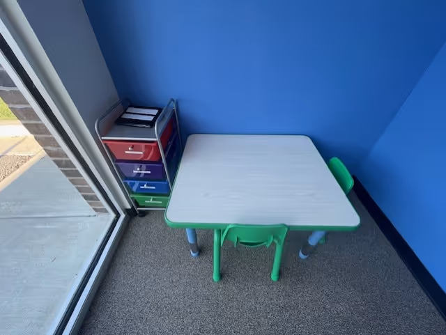 Small child-sized table and colorful drawer storage in a blue therapy room corner.