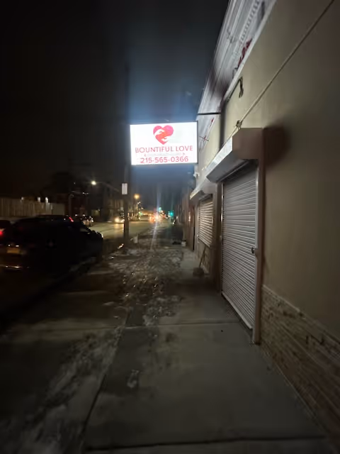 Nighttime sidewalk view of a building exterior with a glowing Bountiful Love sign.