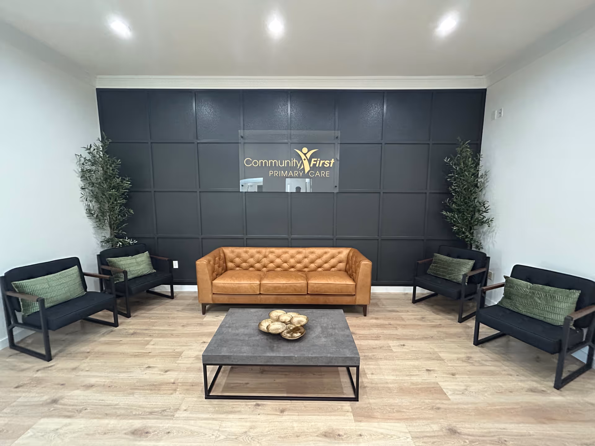 Lobby seating area with tan leather sofa, dark paneled wall, and potted plants.