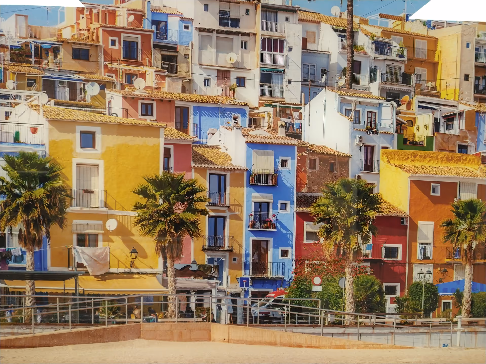 Colorful hillside houses line a sunny street with palm trees.