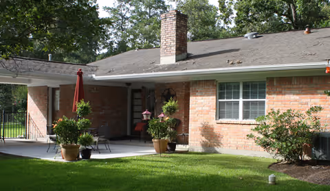 A brick single-story senior living facility with a covered patio and potted plants.