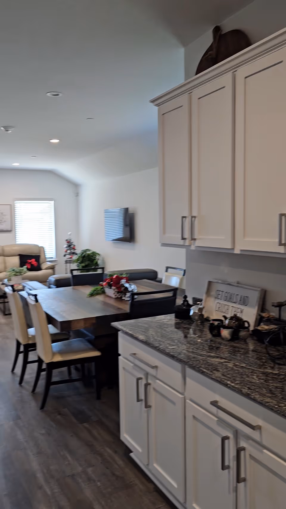 Open kitchen and dining area with white cabinets, granite countertops, and a living room in background.