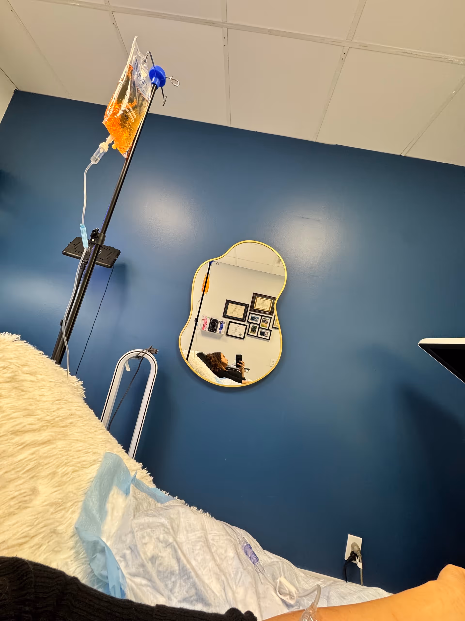 Blue room with an IV drip, hospital bed, and a mirror reflecting a person.