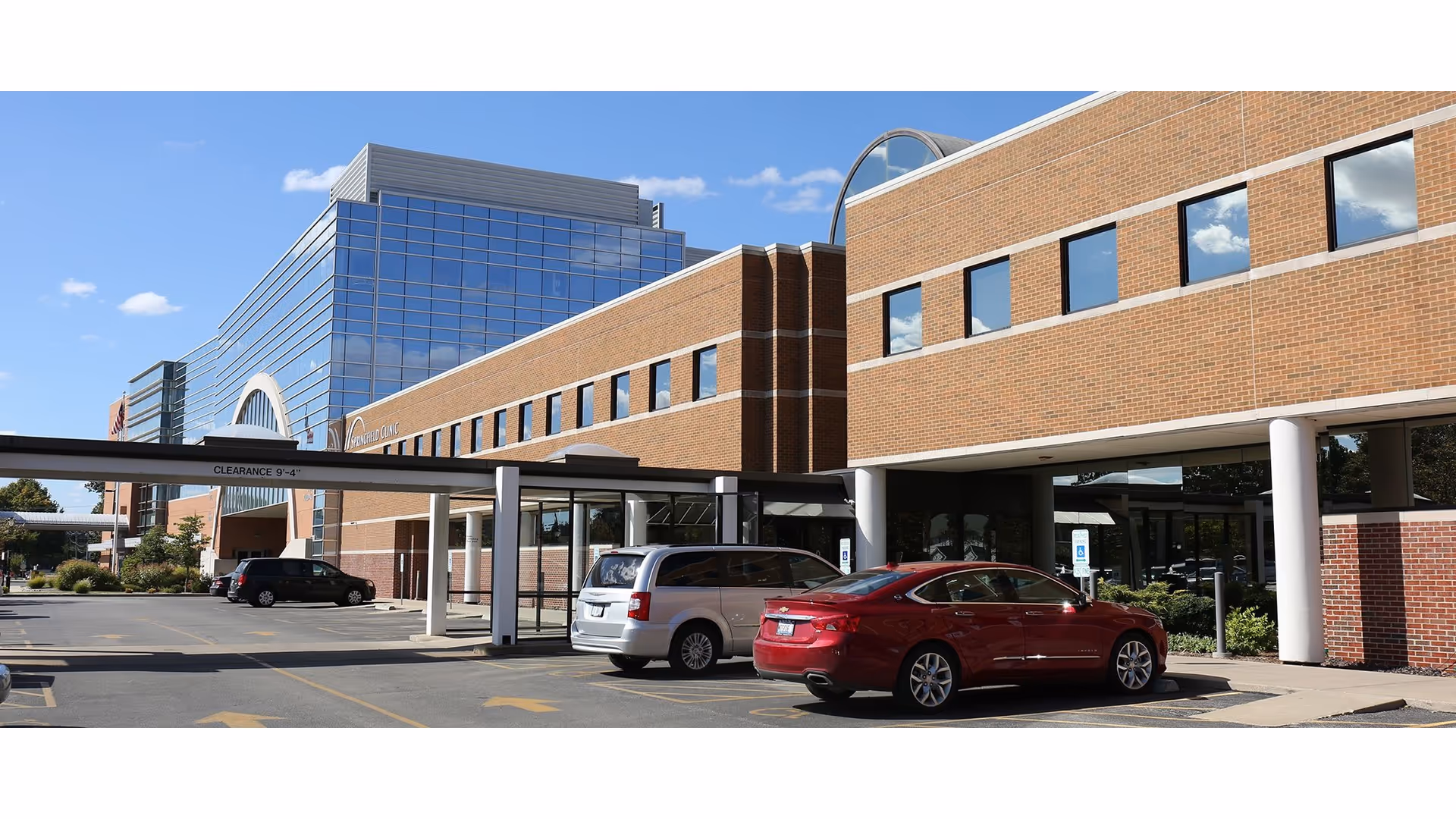 Exterior view of a brick senior living facility with glass windows and parked cars.
