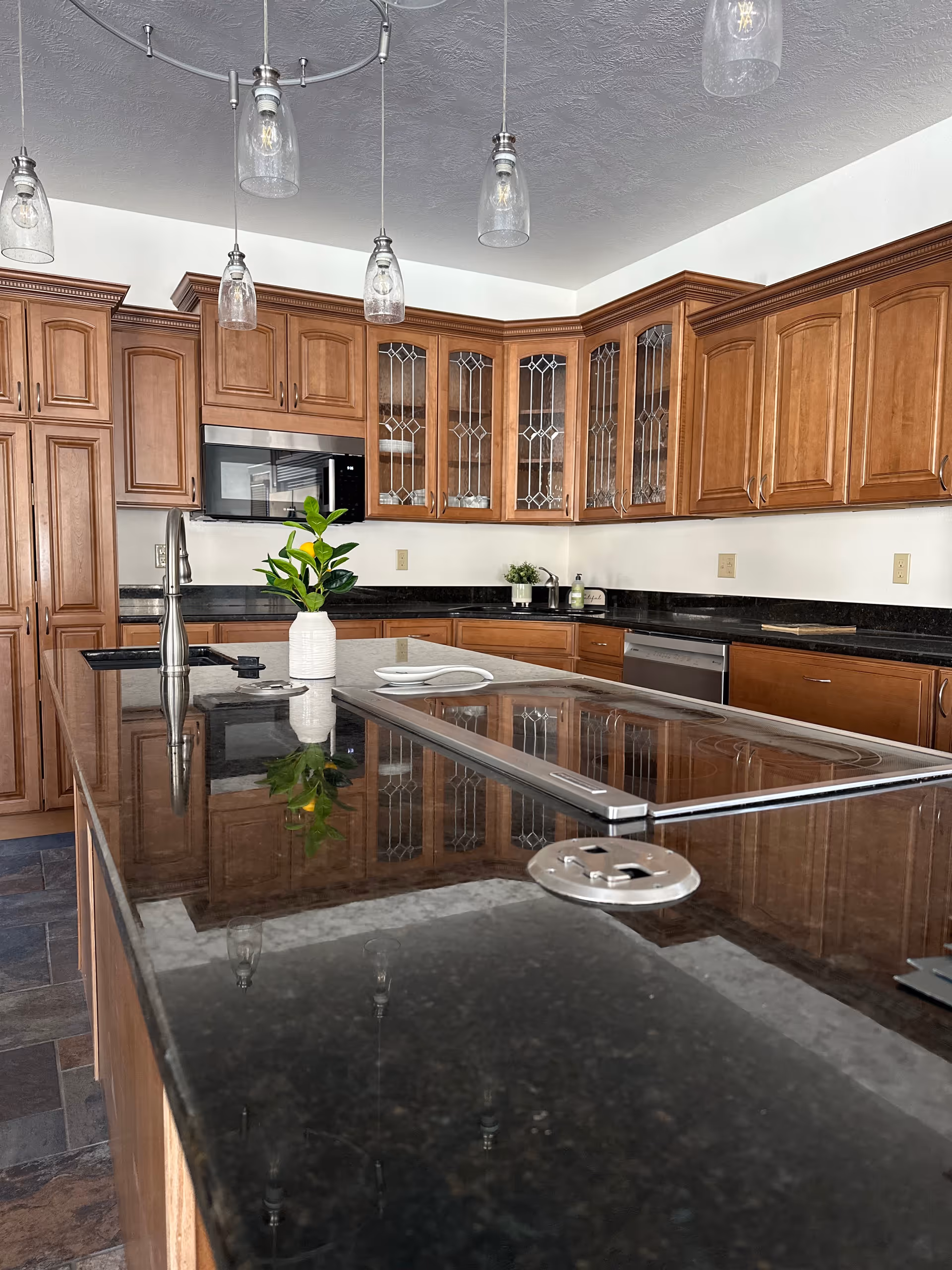 Spacious kitchen with wooden cabinets, dark granite counters, and hanging glass pendant lights.