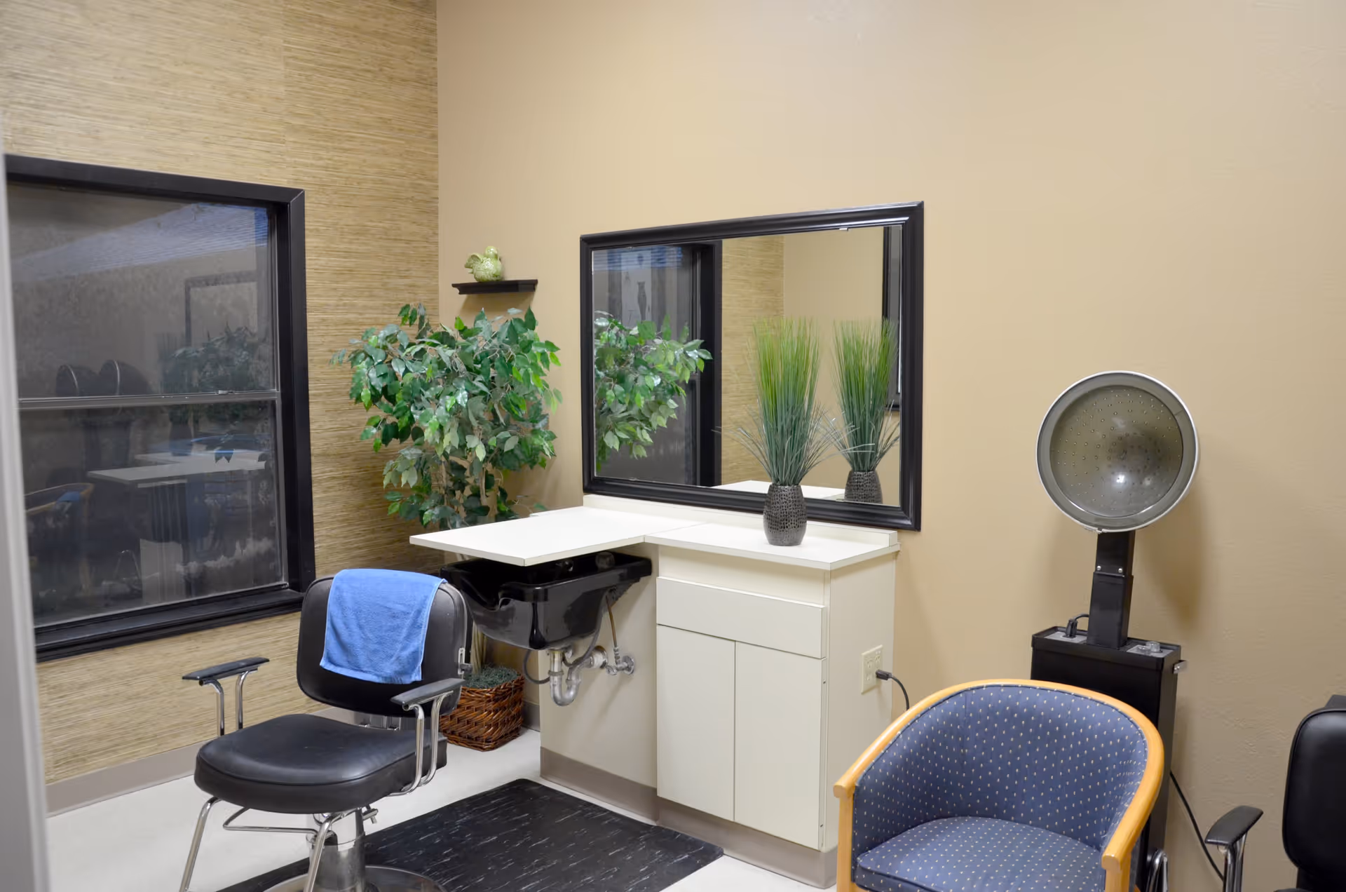 Interior salon room with a styling chair, shampoo sink, large mirror, hooded hair dryer and seating.