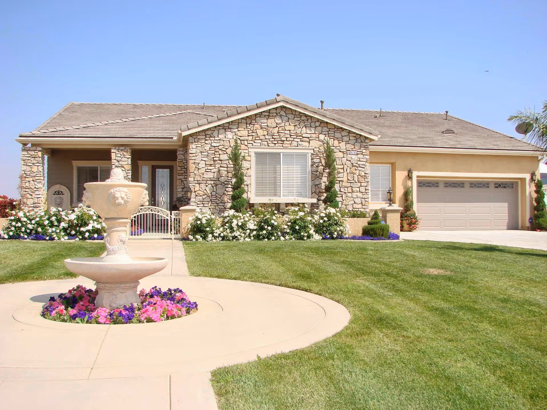 Front exterior of a stone-faced house with a fountain and manicured lawn.
