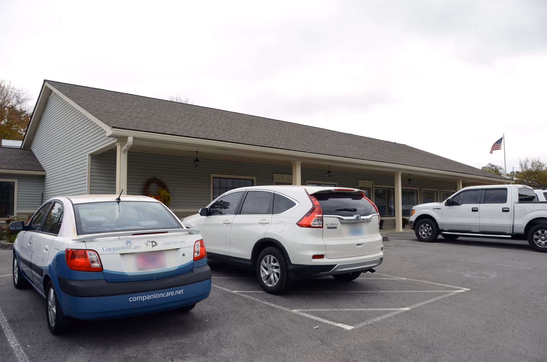 Exterior view of a single-story facility with a covered entrance and parked cars.