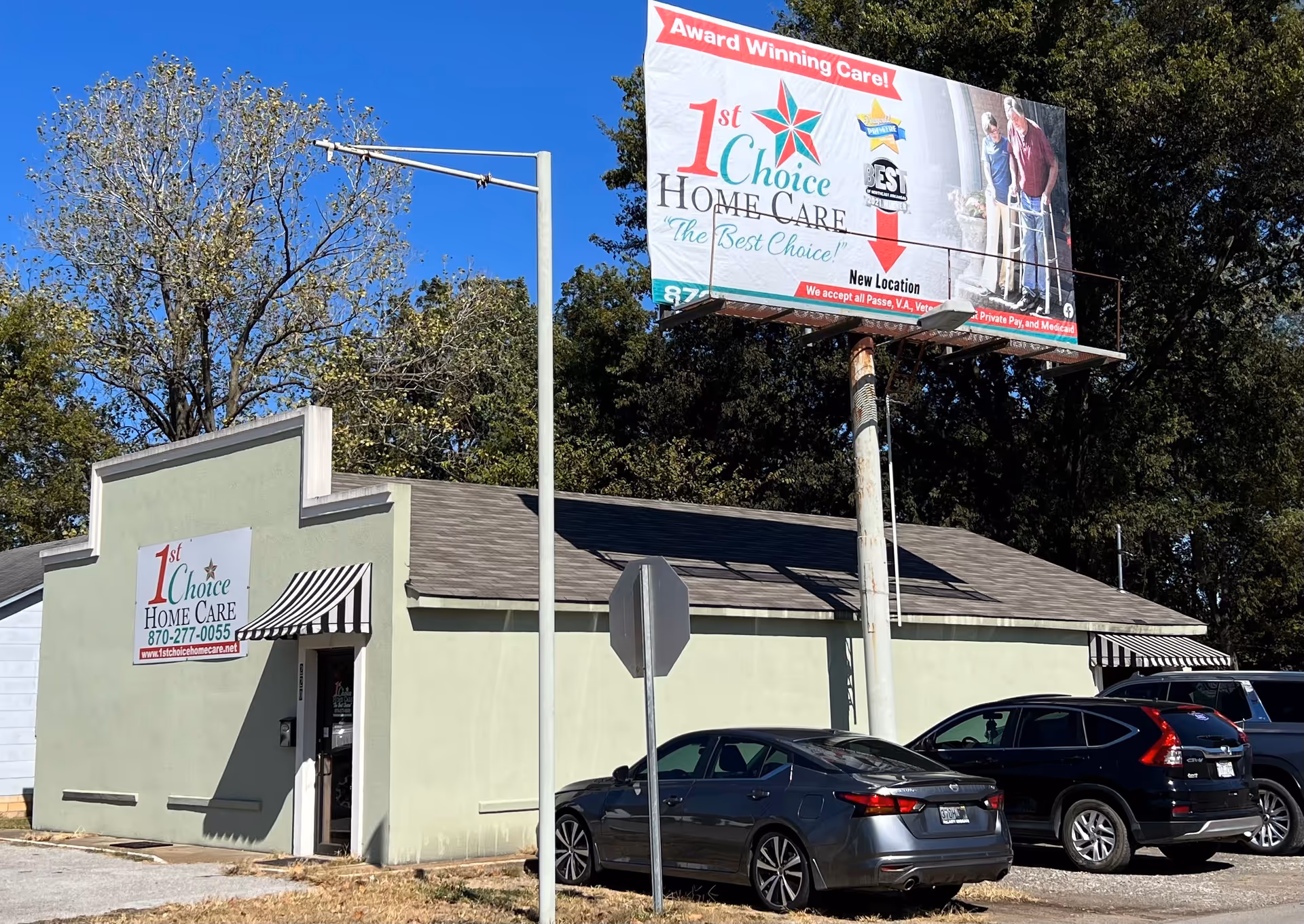 Small light-green building labeled '1st Choice Home Care' with a large billboard and parked cars.