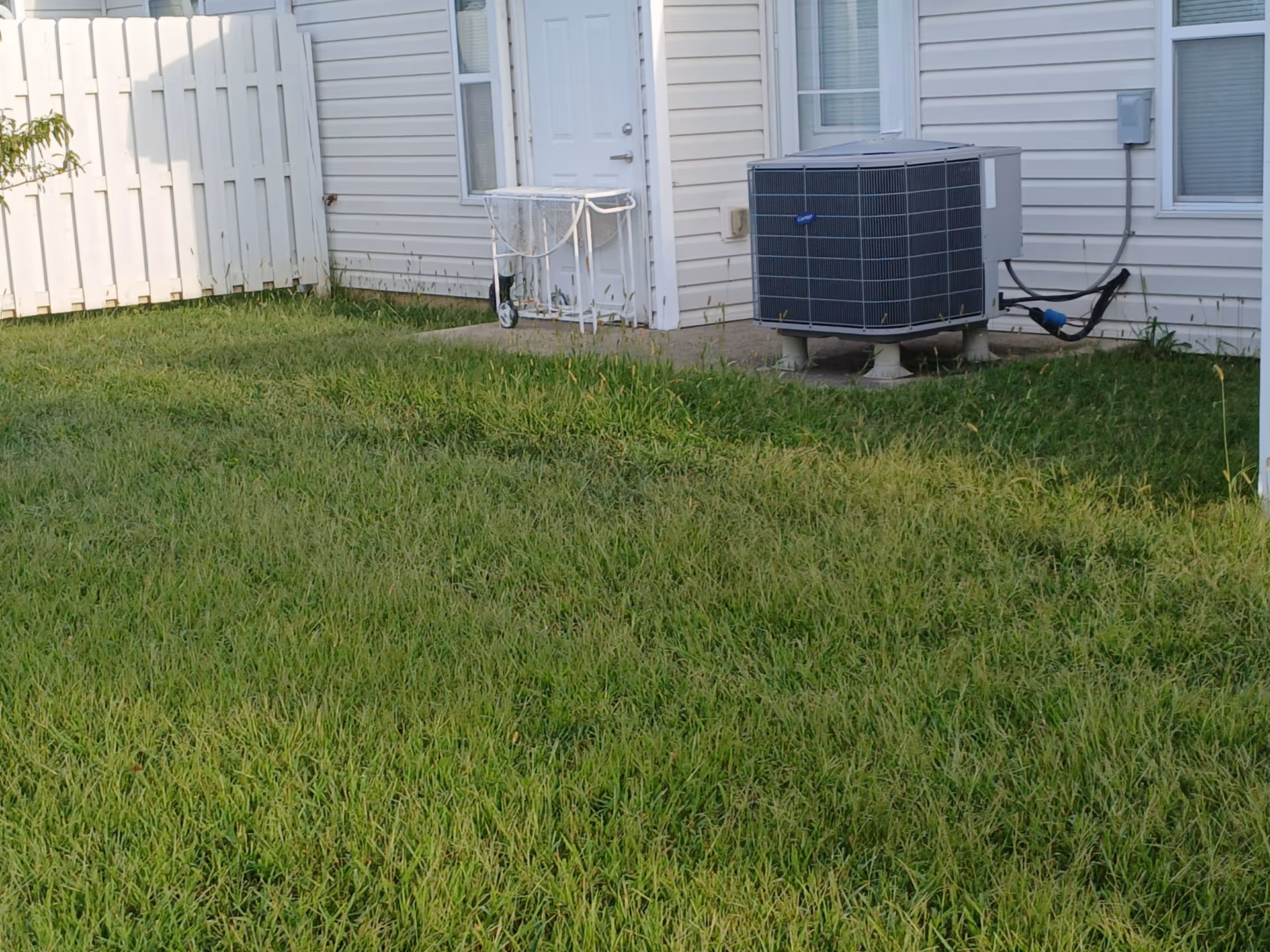 Back exterior of a beige house with an air conditioner on a concrete pad in grass.