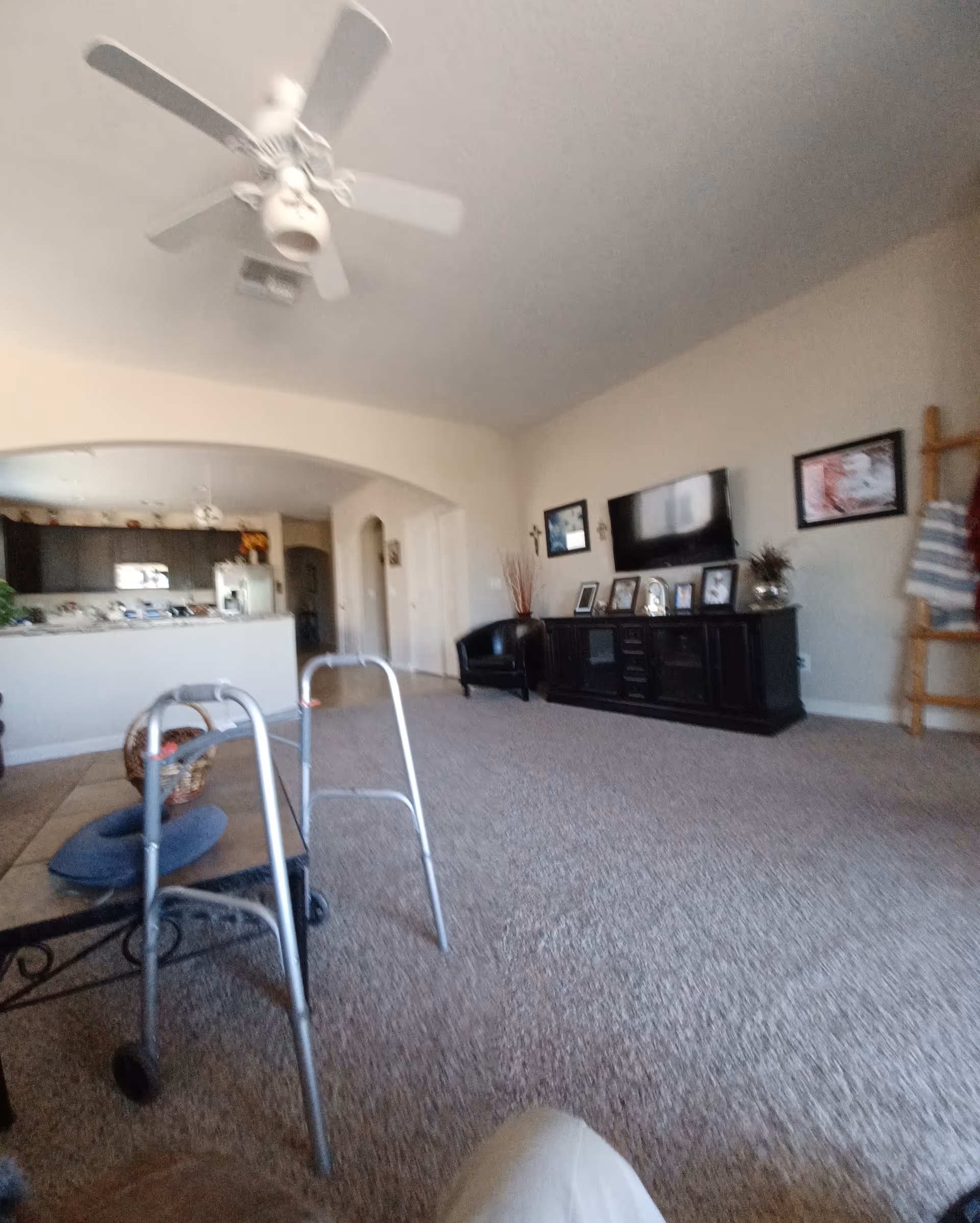 Spacious living room with ceiling fan, TV, photos, and a walker by the coffee table.