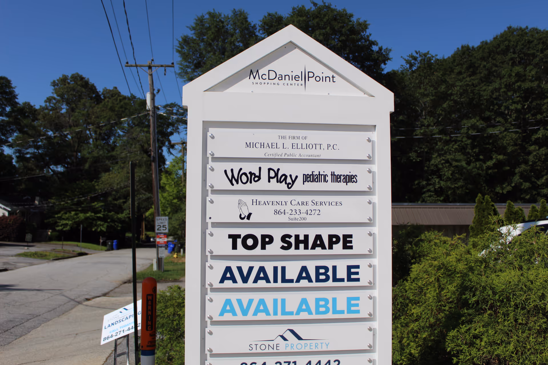 A tall white outdoor signboard listing Heavenly Care Services among other business names along a street.