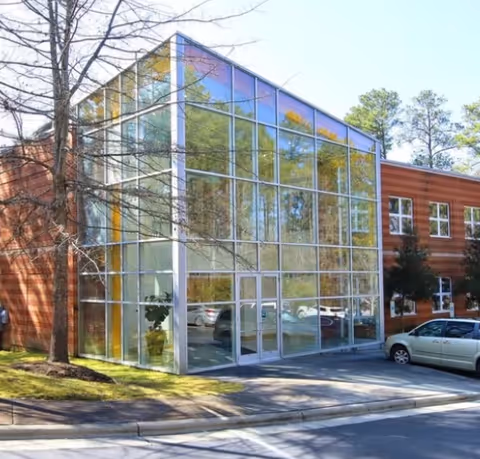 Glass-front entrance to a brick senior living facility with parked cars.
