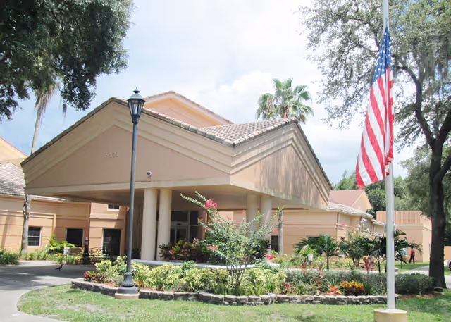 Front entrance of Palm Terrace Assisted Living Facility with landscaped garden and flag.