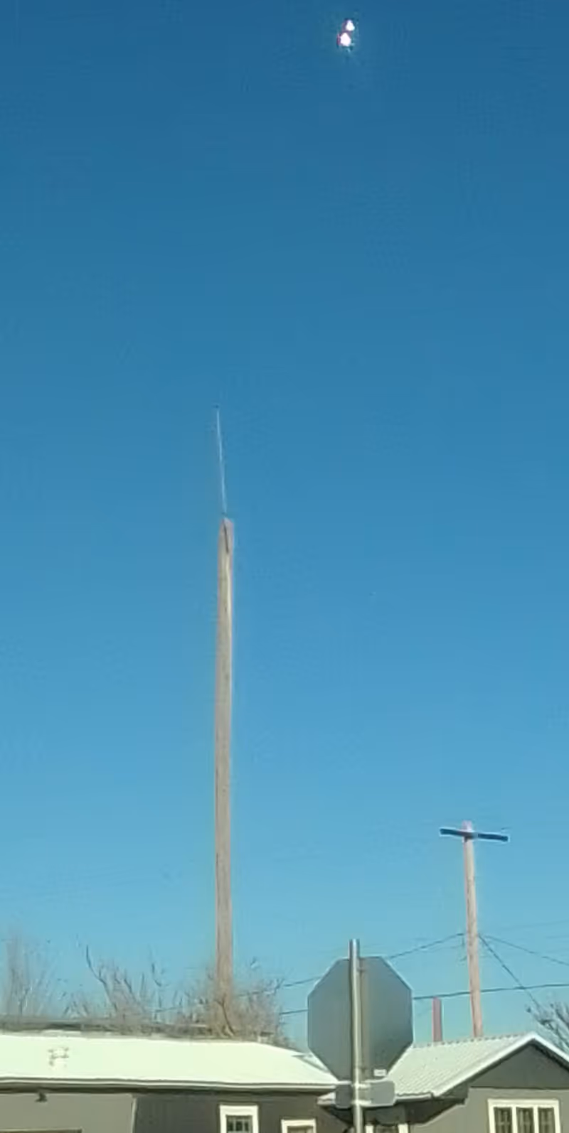 Clear blue sky above a street with utility poles, a stop sign, and rooftops.