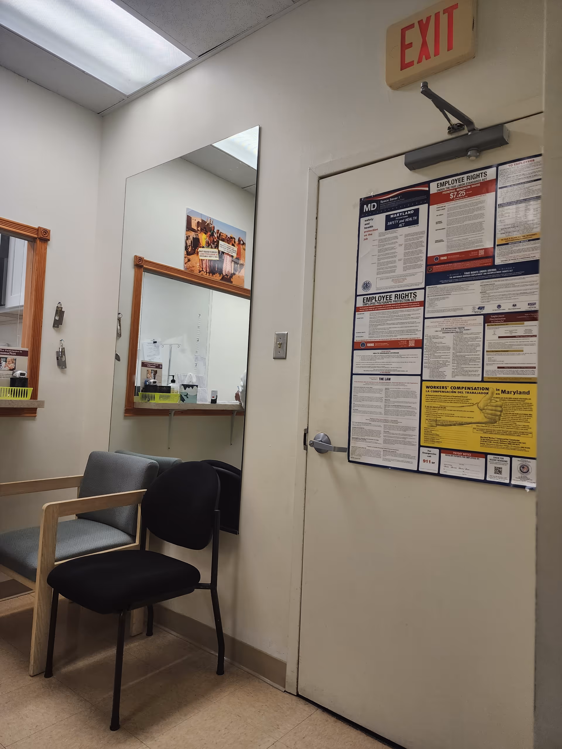 Interior waiting area with chairs, a mirror, posters, and an exit door.
