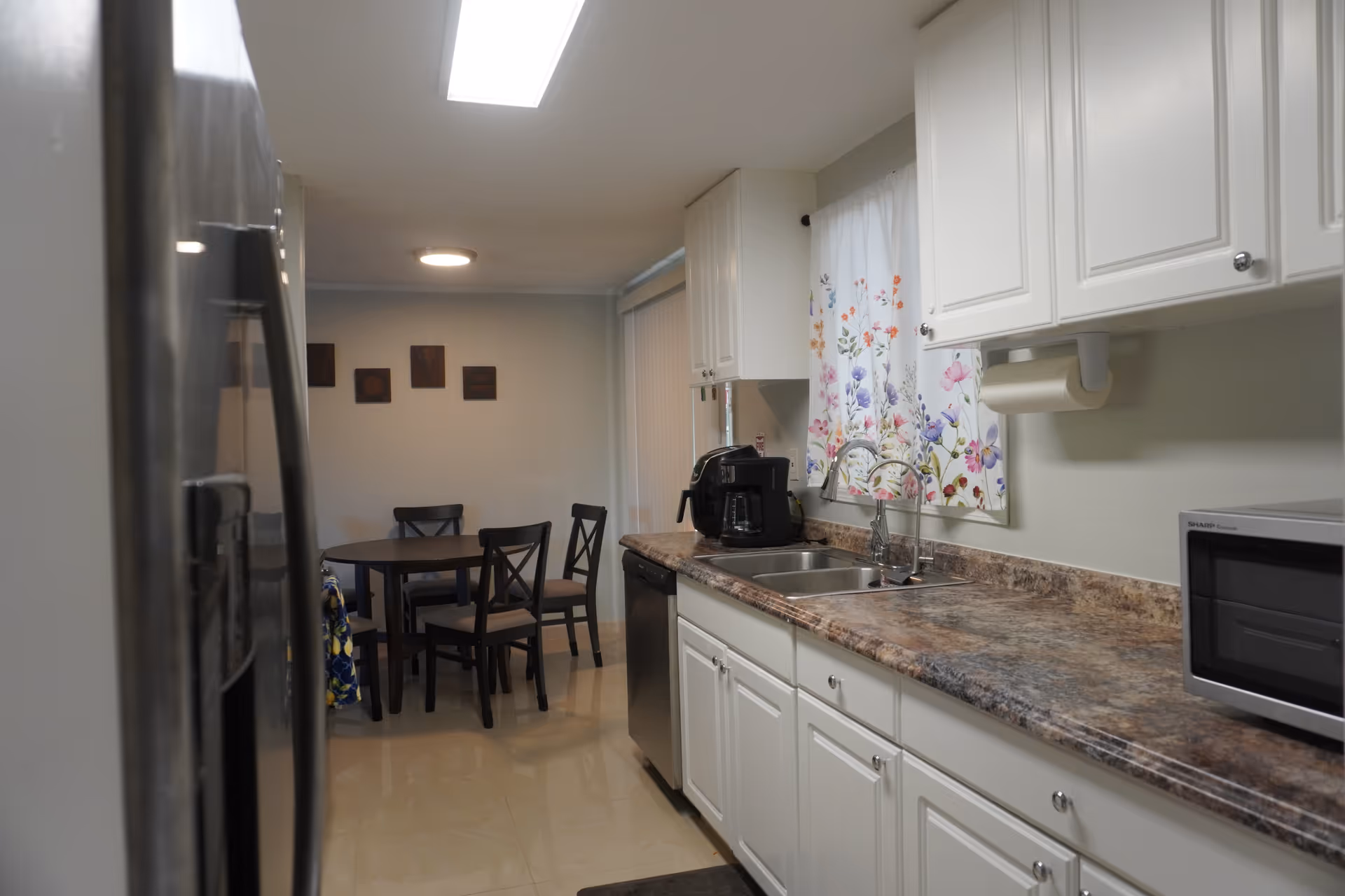 Bright kitchen with white cabinets, marble countertops, sink, microwave, and a dining area in back.