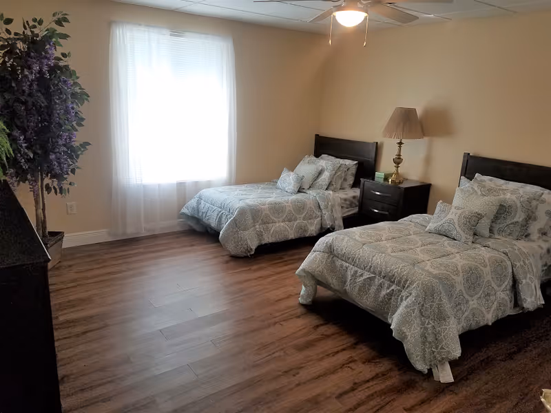 Two twin beds with a nightstand, lamp, and window in a bright bedroom.