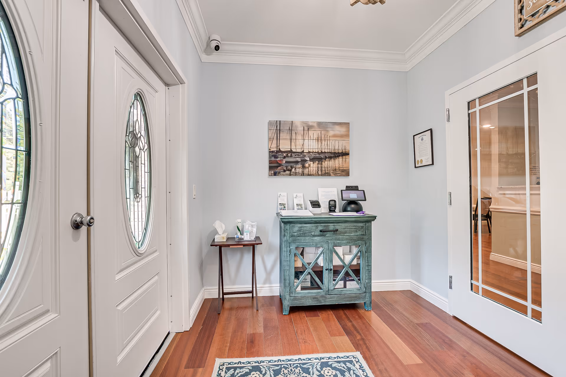 Entry foyer of a memory care facility with a front door, turquoise console, and wooden floor.