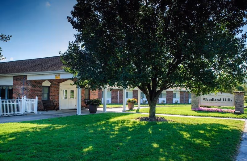 Exterior view of Woodland Hills facility with a brick entrance, tree, and lawn.
