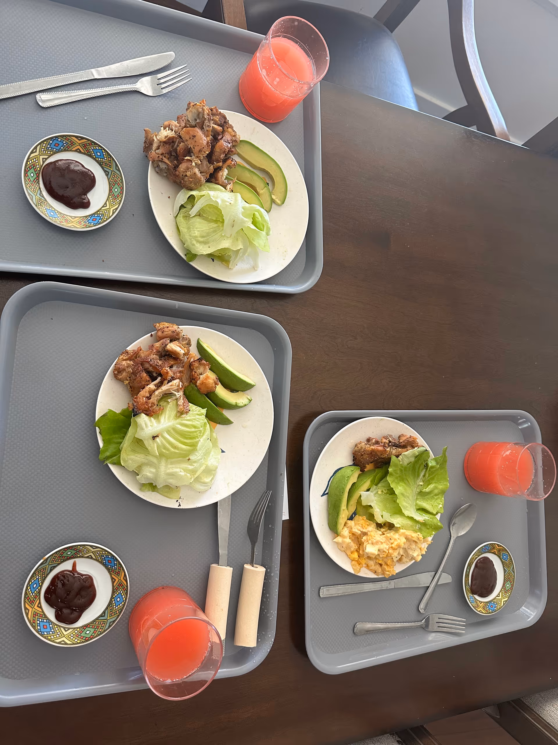 Trays with plated meals and pink beverages on a dining table in a senior living facility.