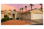 Front view of a beige, single-story senior residence with a two car garage and palm trees.