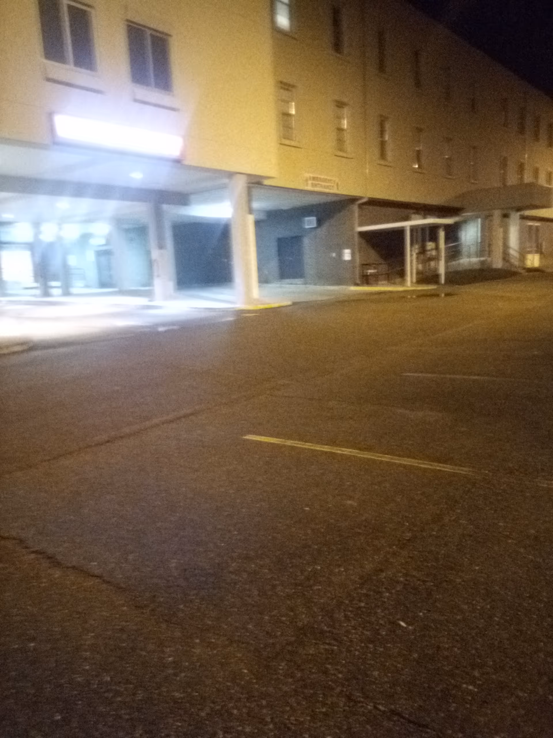 Night exterior of a multi-story building with a covered entrance and dimly lit parking area.