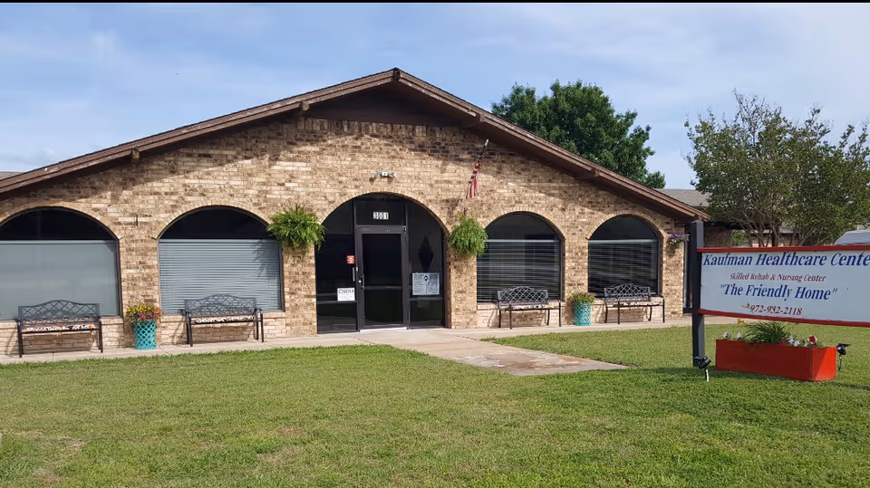 Single-story brick healthcare center with arched windows, benches, and a green lawn in front.