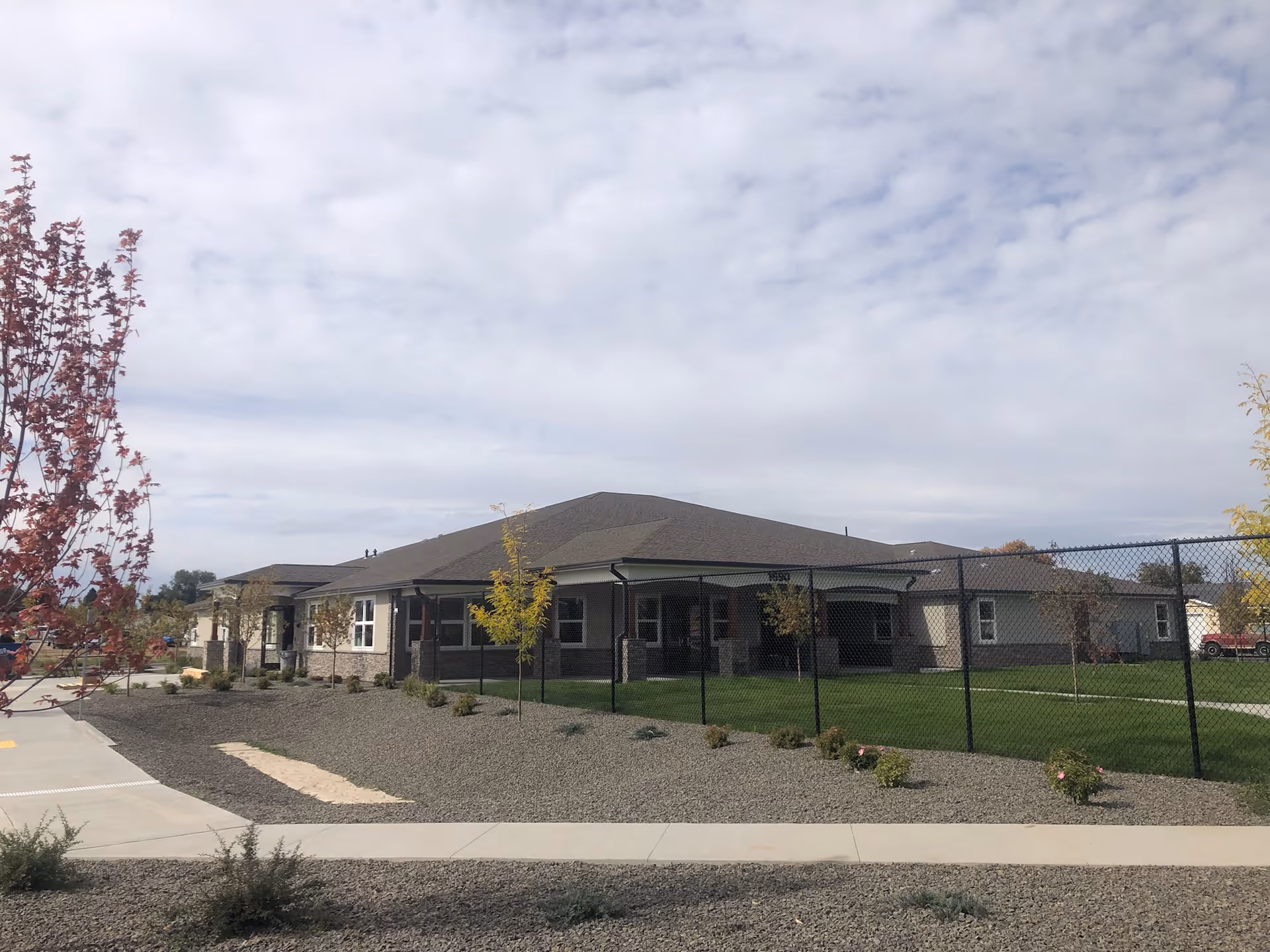 Exterior of a single-story memory care facility with a fenced lawn and gravel landscaping.