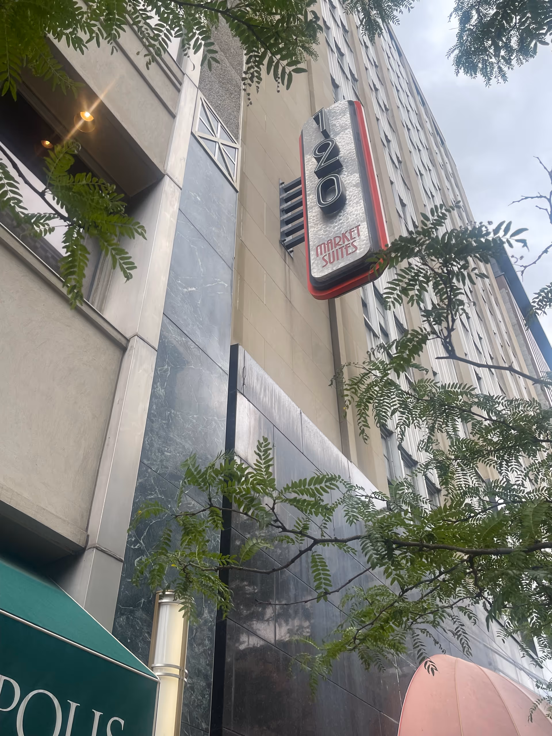 Tall building exterior with a vertical Market Suites sign and tree branches.