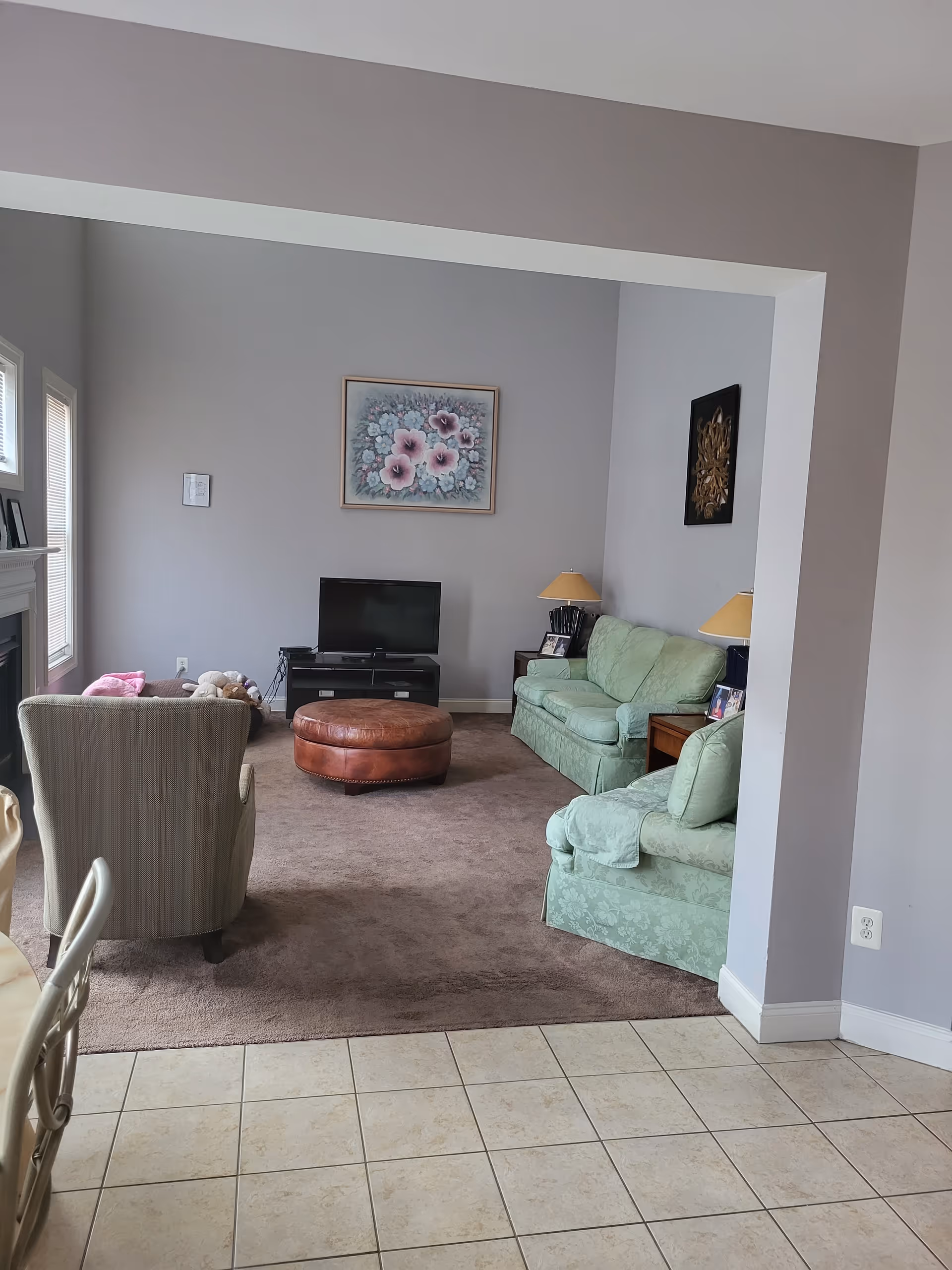 Cozy living room with pastel walls, green sofas, chairs, ottoman, and a TV.