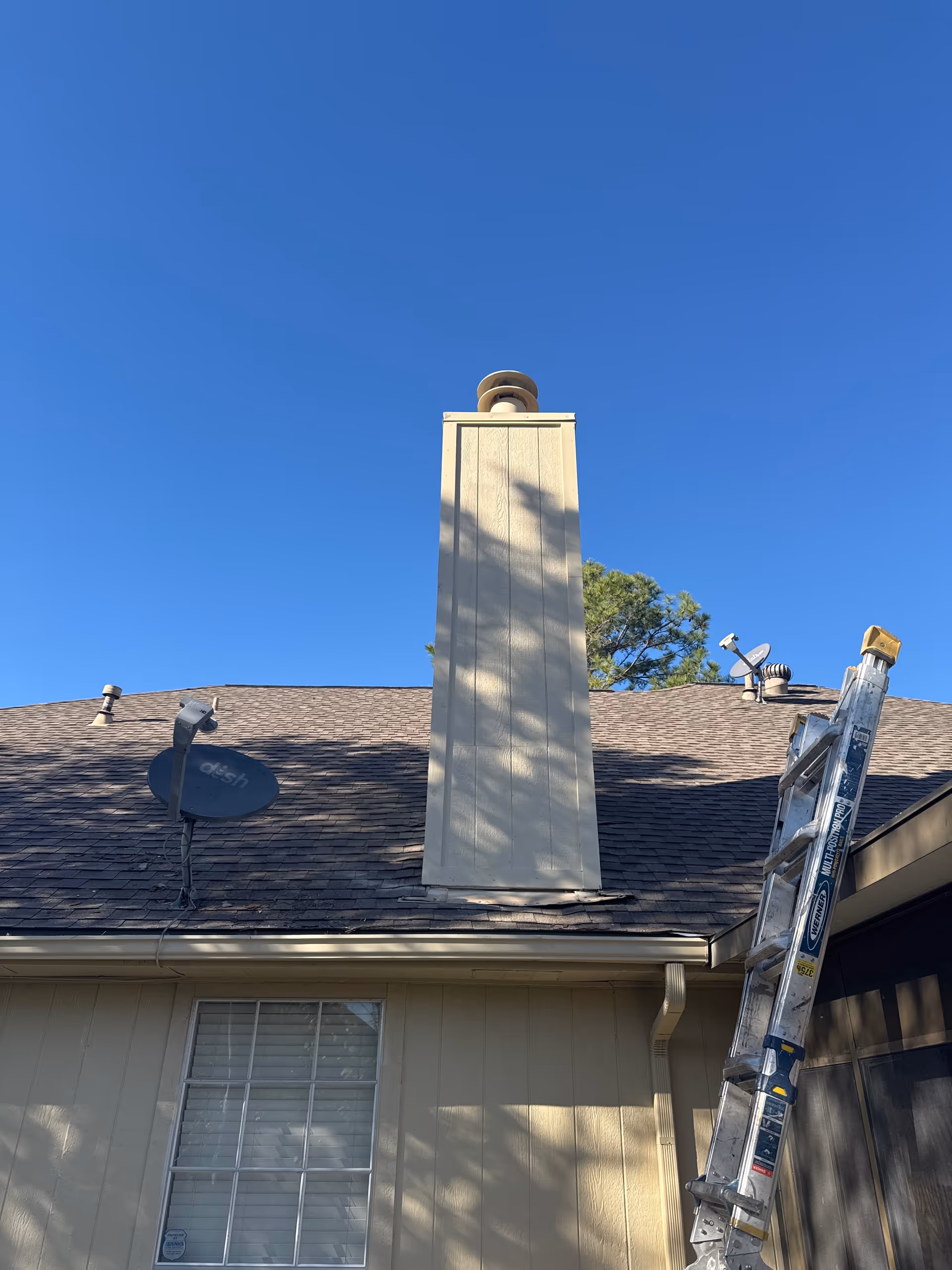 Blue sky over exterior of senior living facility, chimney, satellite dish, and ladder.