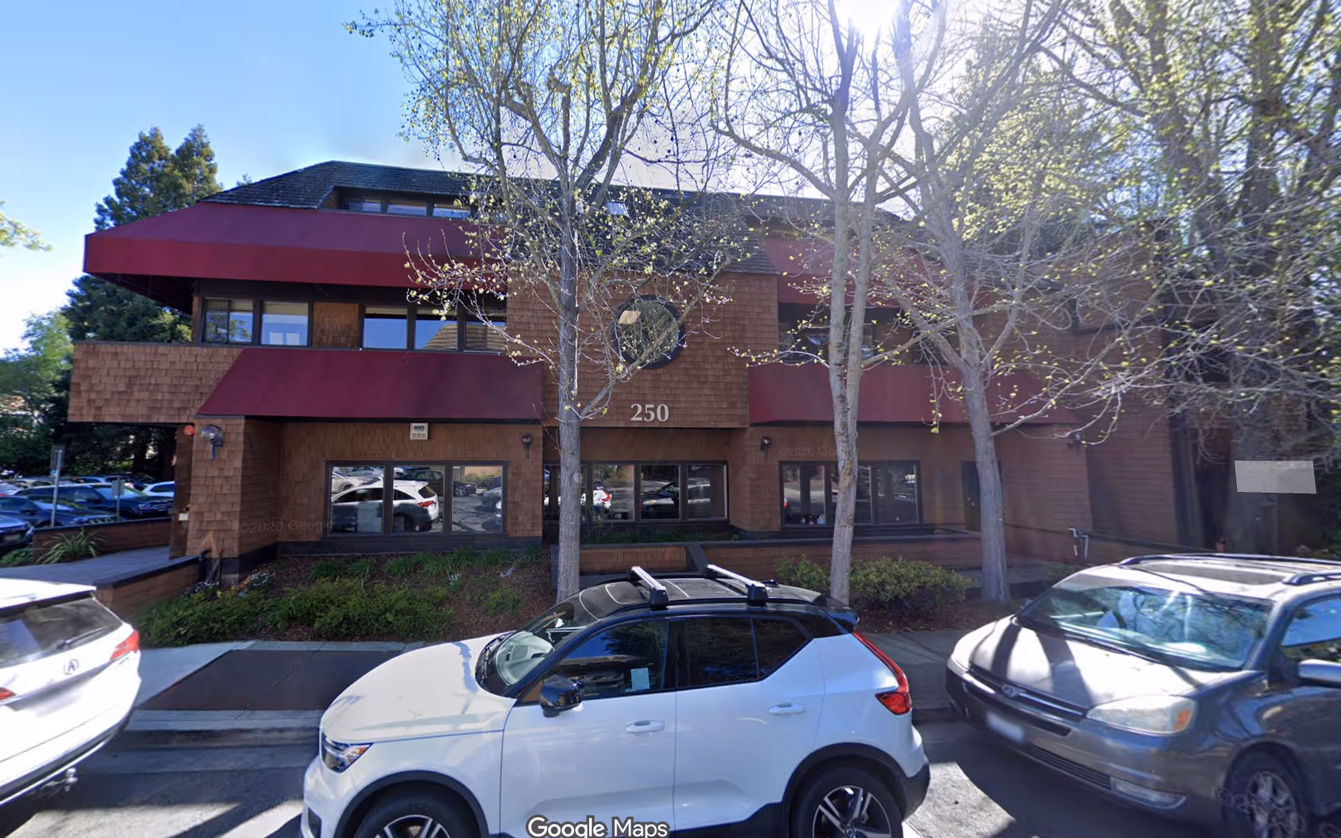 Two-story brick building with red awnings, windows, and several parked cars.
