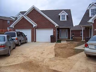 Front exterior of a brick senior living building with garages and parked cars.