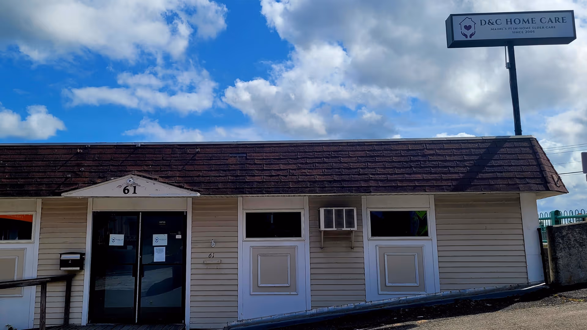 Small single-story facility exterior with front doors, windows, and a D&C Home Care sign.