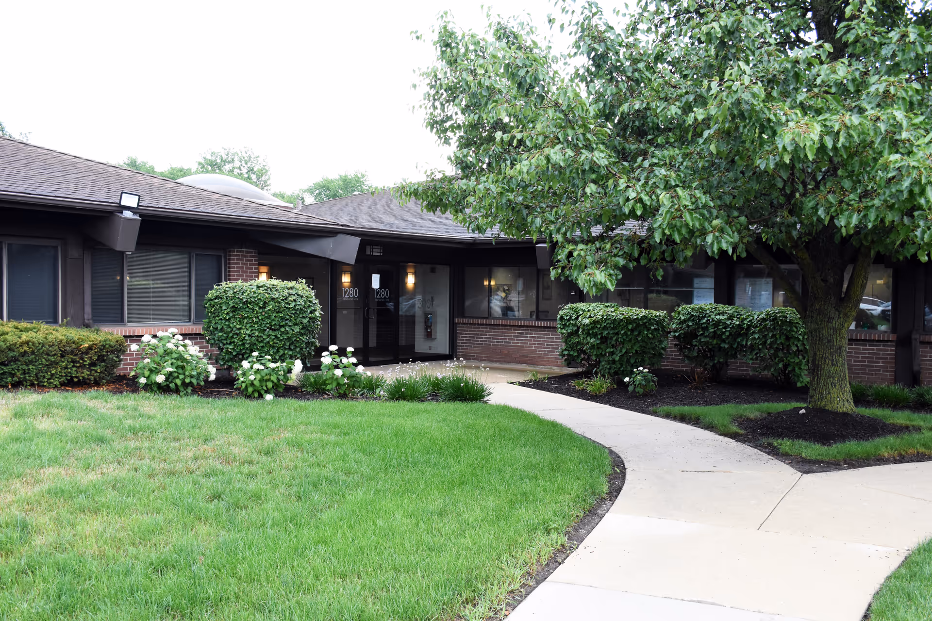 Exterior view of a senior care facility entrance with curved walkway and landscaped grounds.
