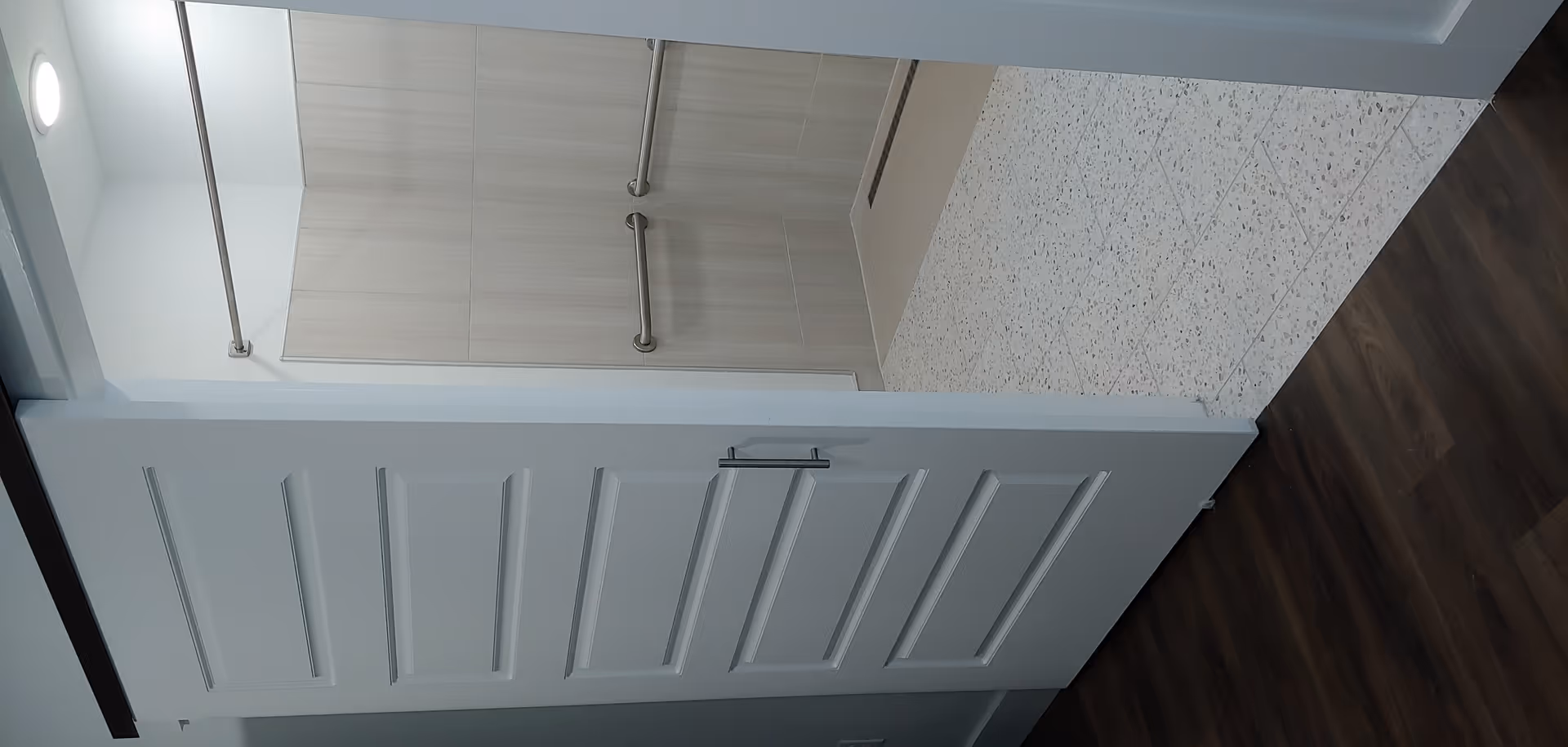 Accessible bathroom with tiled walls, grab bars, and an open doorway from a dark wood hallway.