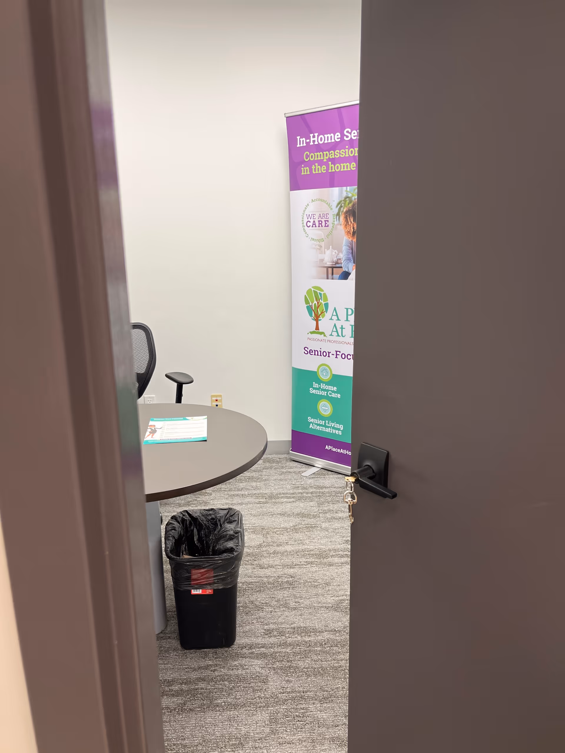 Open door reveals a small office with a round table, banner, and trash can.