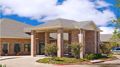 Brick-clad senior living facility entrance with columns and a covered drop-off area.