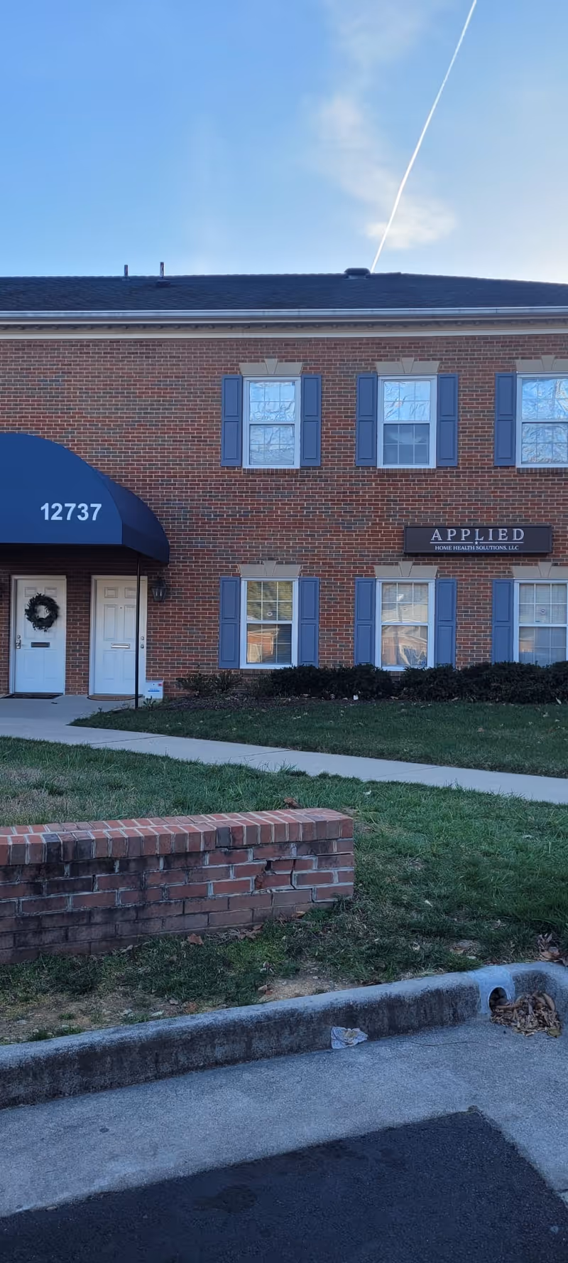 Brick building exterior with blue shutters, awning, and Applied Home Health Solutions sign.