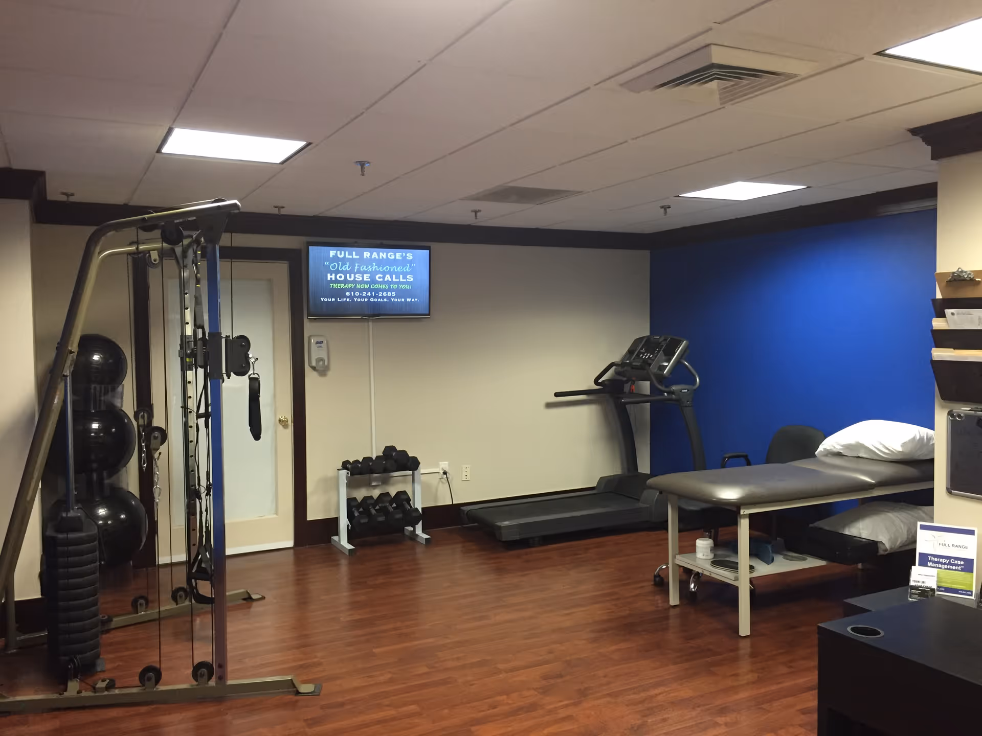 Interior fitness room with treadmill, weight stack, and therapy table.
