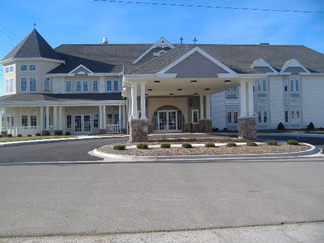 Front exterior of a large two-story senior living building with a covered drop-off porte-cochère and circular driveway.