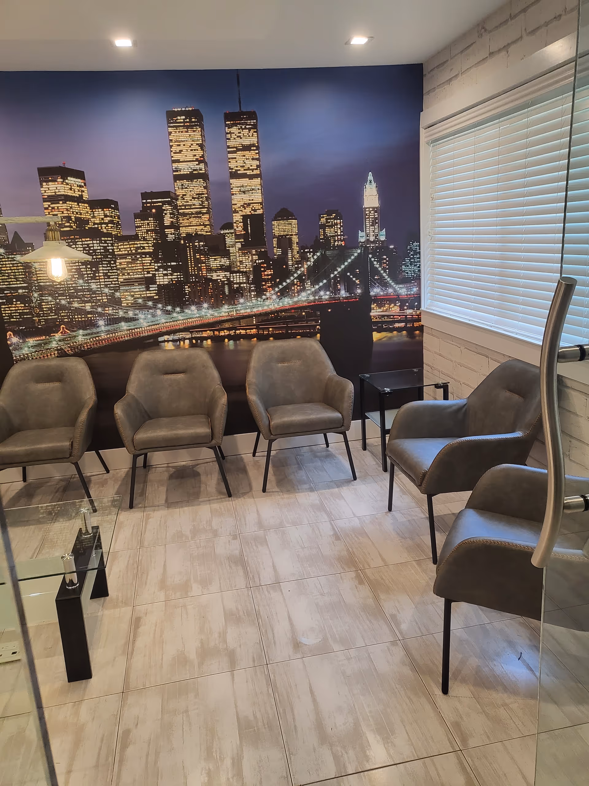 Indoor waiting area with gray chairs and a city skyline mural.
